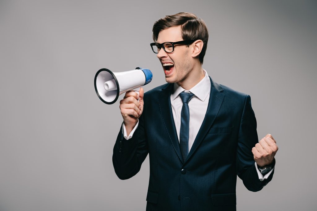 angry businessman in suit screaming in megaphone on grey background