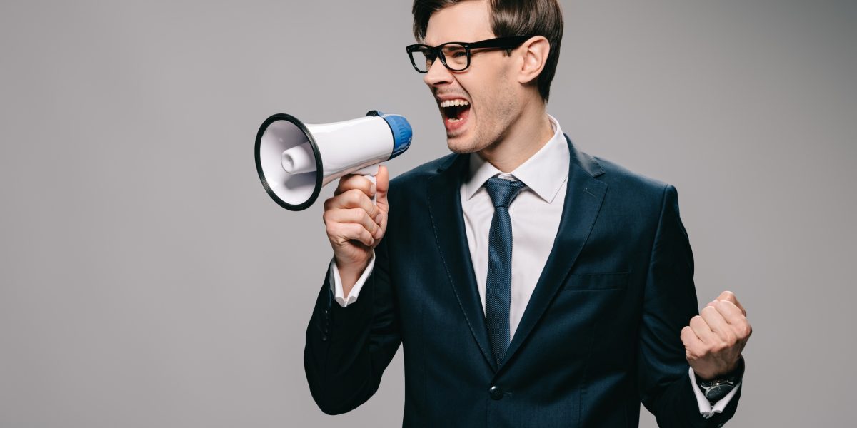 angry businessman in suit screaming in megaphone on grey background