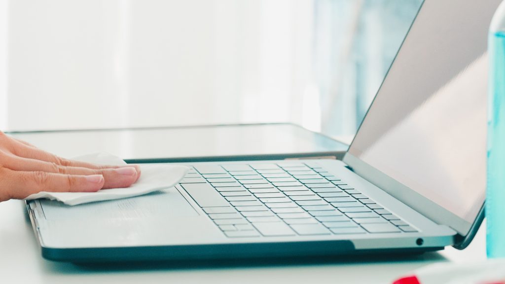 Asian woman using alcohol spray on tissue clean laptop before open for protect coronavirus.