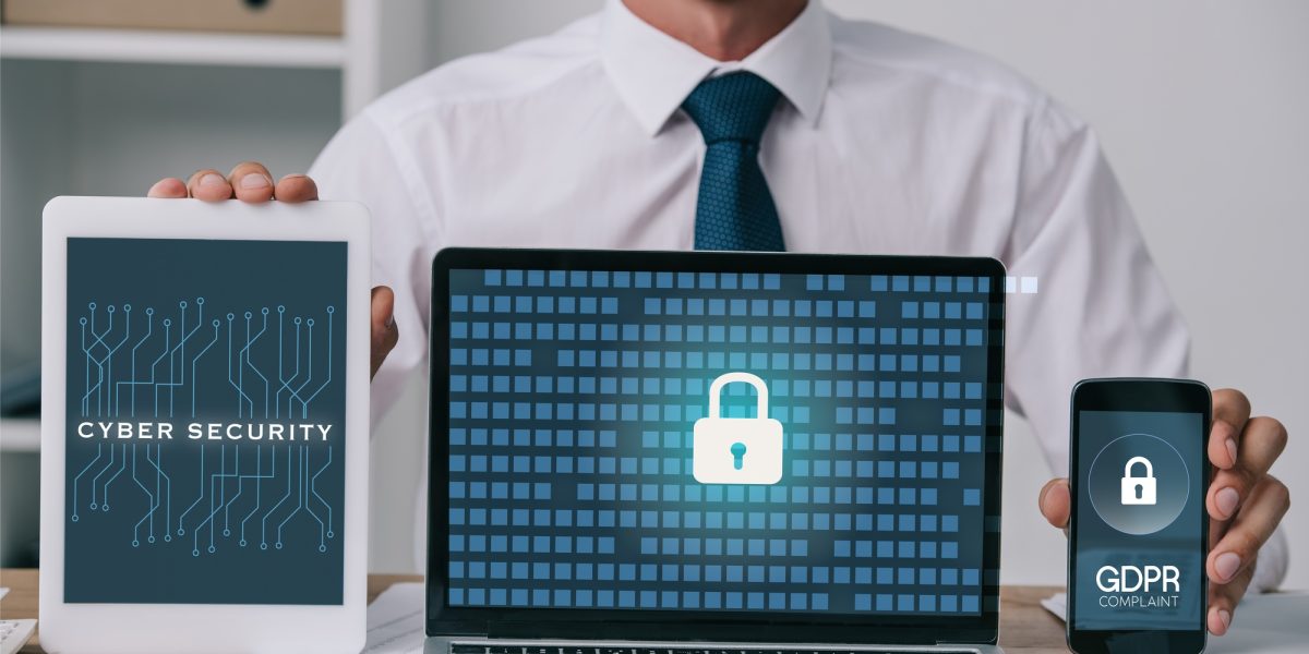 cropped shot of businessman showing laptop, tablet and smartphone with gdpr and cyber security signs