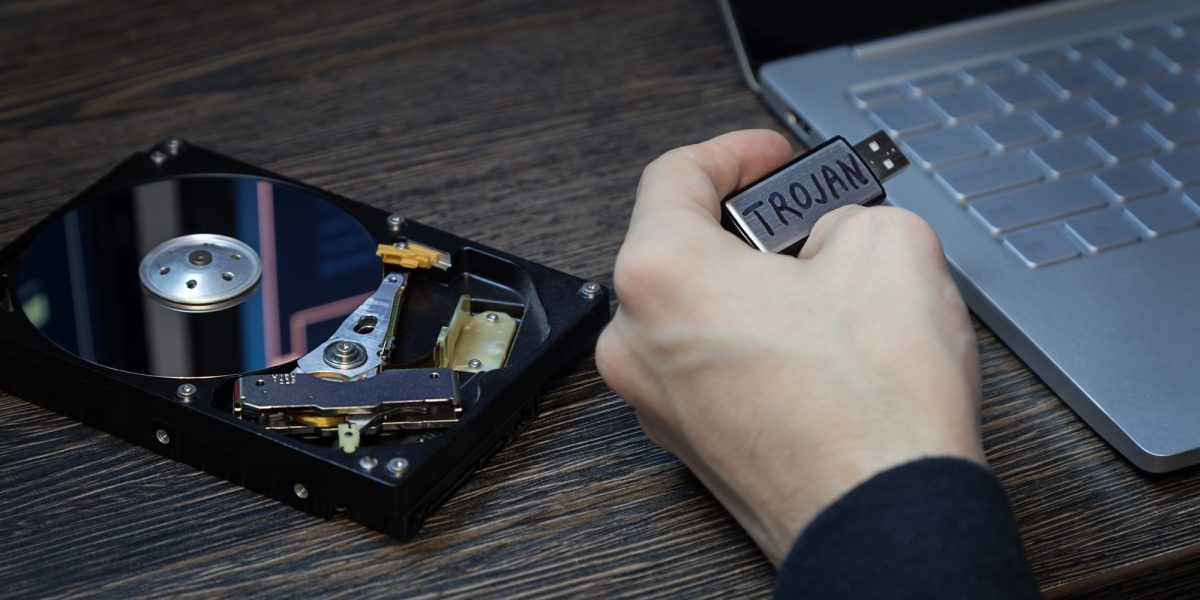 Man's hand with a flash drive infected with a virus and an open laptop on the desk