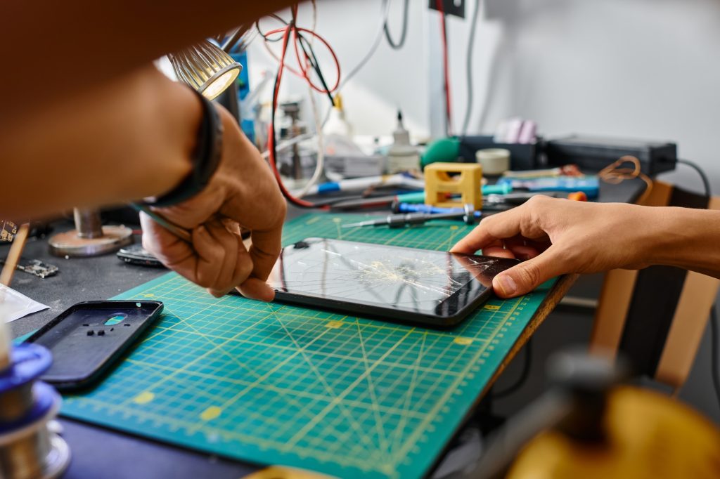 partial view of experienced technician removing broken touchscreen of digital tablet in workshop