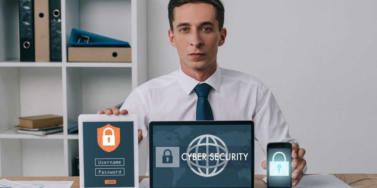 portrait of businessman showing laptop, tablet and smartphone with cyber security signs on screens