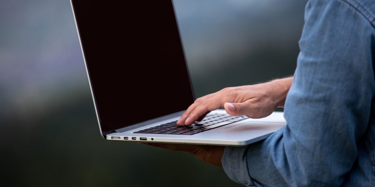 Man working outdoors with laptop in mountains. Concept of remote work or freelancer lifestyle