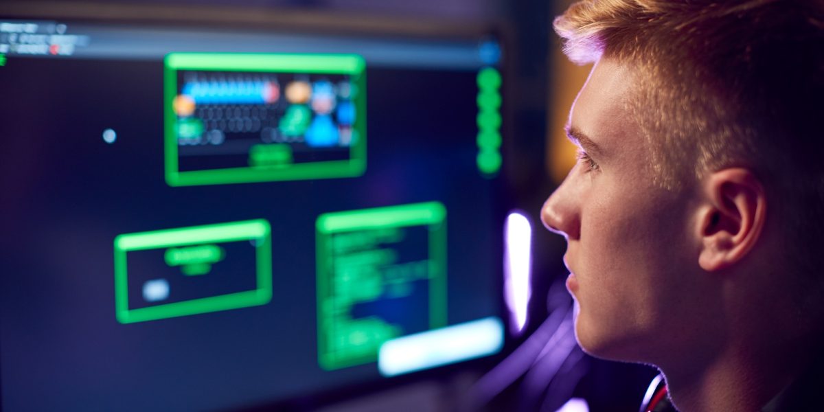 Male Teenage Hacker Sitting In Front Of Computer Screens Bypassing Cyber Security